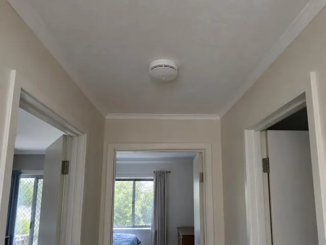 Ceiling smoke alarm in a hallway with white trims and adjoining rooms in Benowa